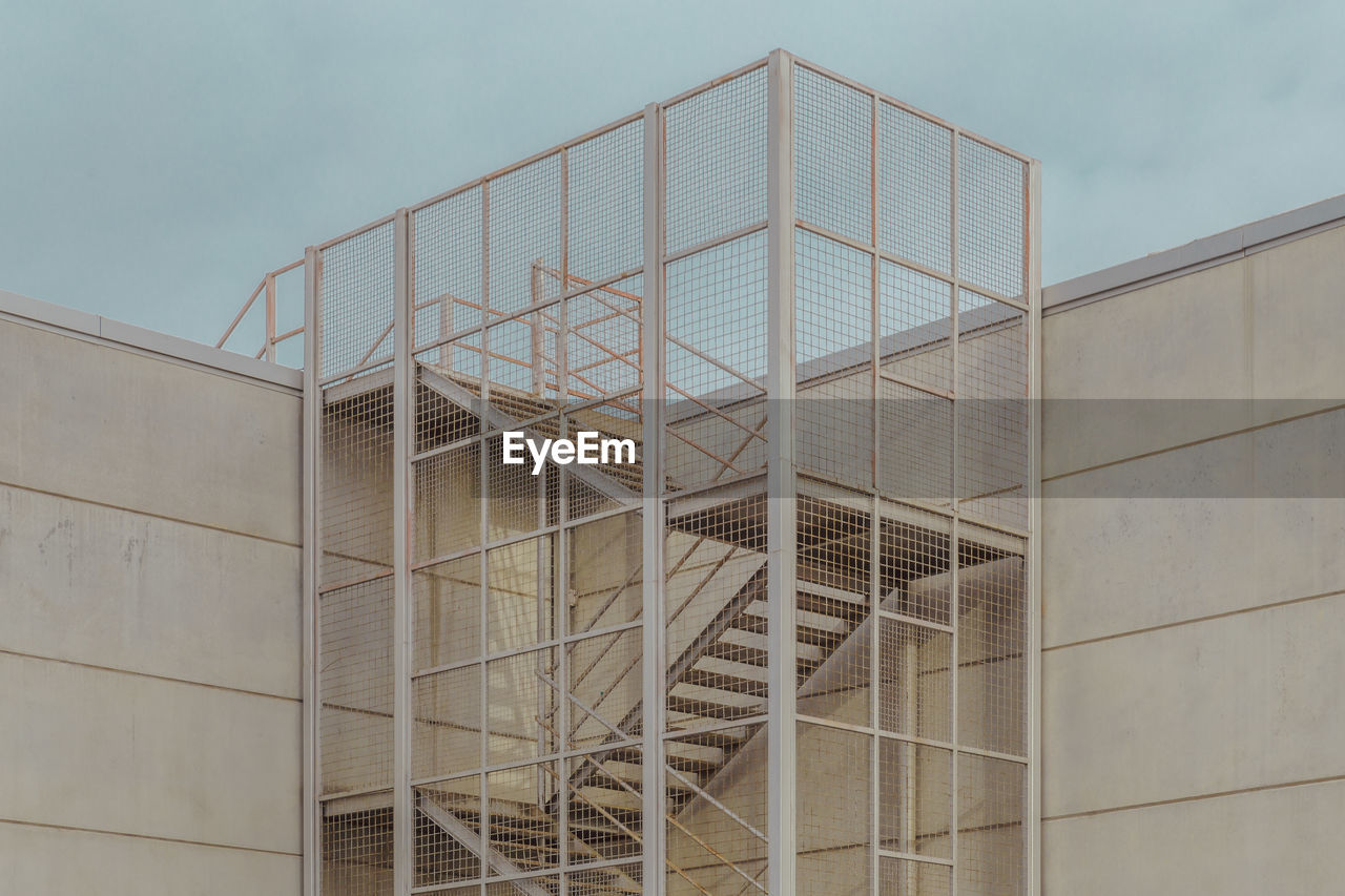 Metallic industrial ladder on wall against sky