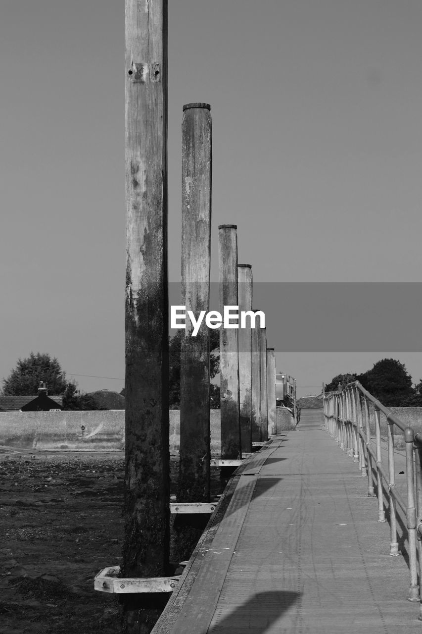 WOODEN POSTS ON FOOTPATH BY WATER AGAINST CLEAR SKY