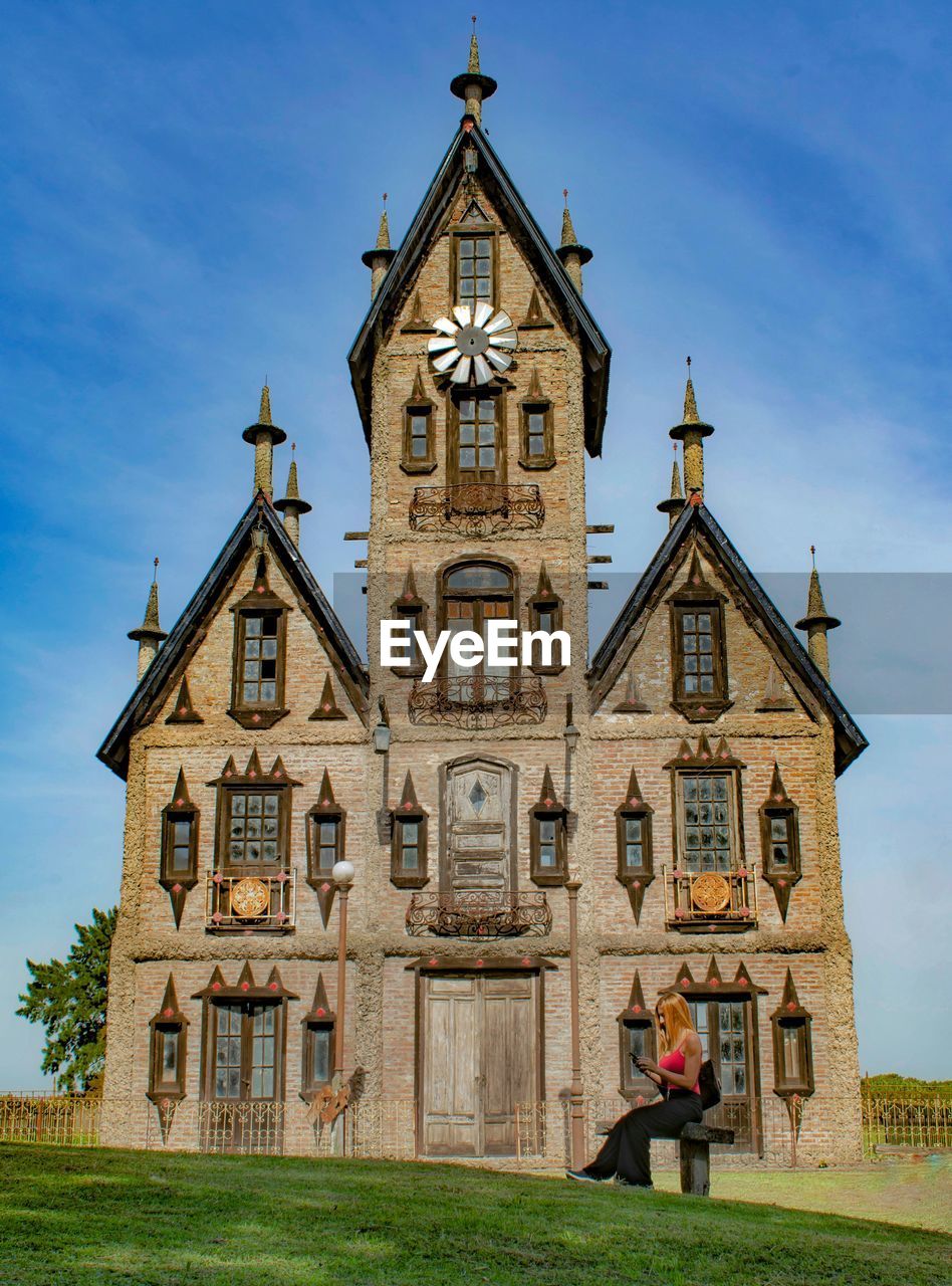 Woman using smart phone while sitting against historic building