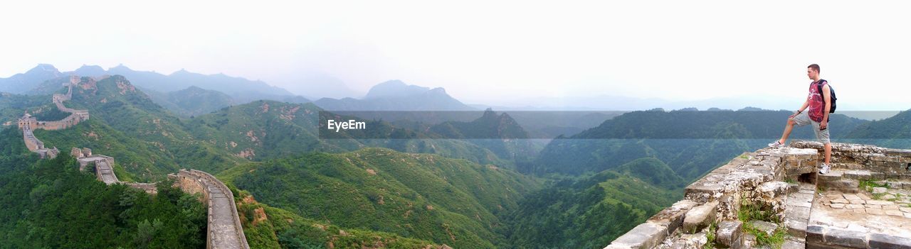 Panoramic view of man at mountain peak looking at great wall of china