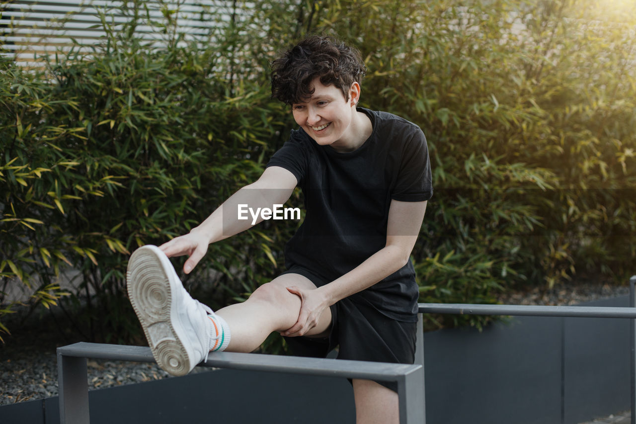 YOUNG MAN LOOKING AWAY WHILE SITTING BY RAILING