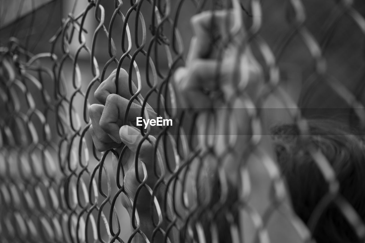 Close-up of hands on chainlink fence