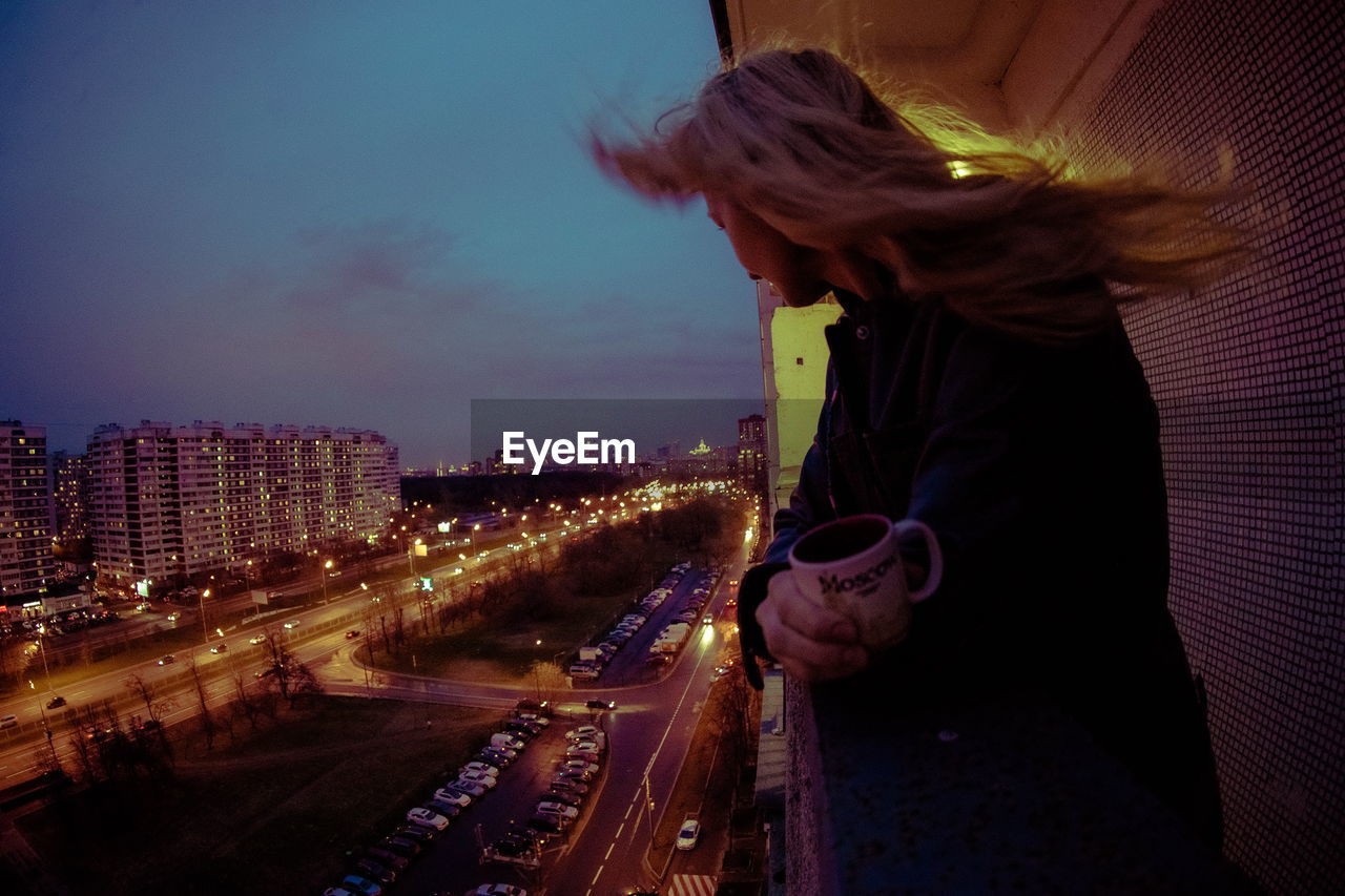 Side view of woman with mug looking towards city from balcony