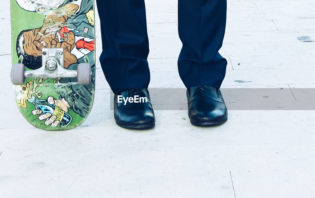 Low section of man standing by skateboard on footpath