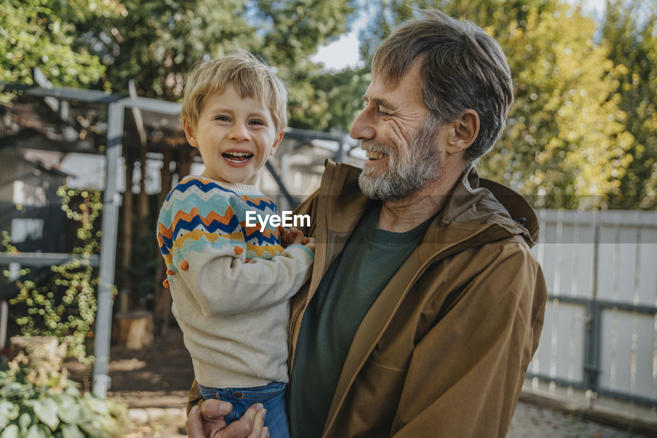 Father laughing while carrying son standing in back yard on sunny day