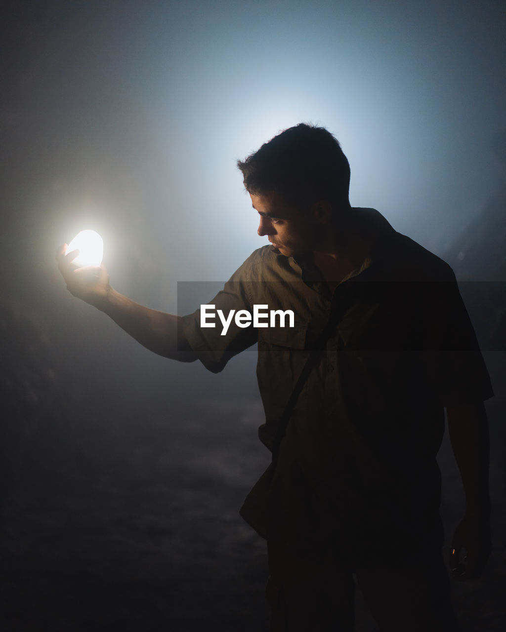 Young male speleologist with bright flashlight in hand exploring dark subterranean cave during extremal adventure