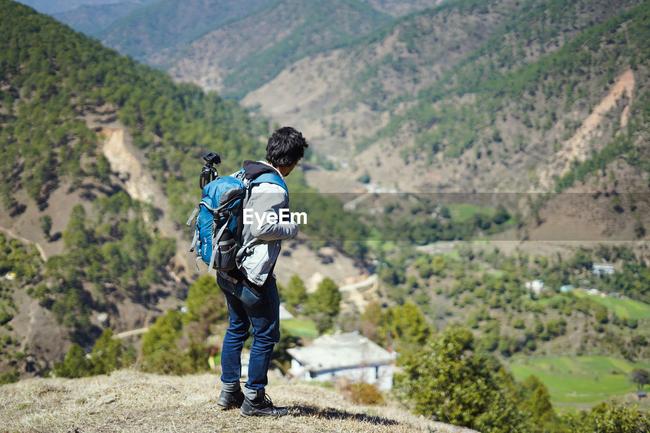 Young handsome indian boy standing on the top of the mountain with a bag pack , traveling 