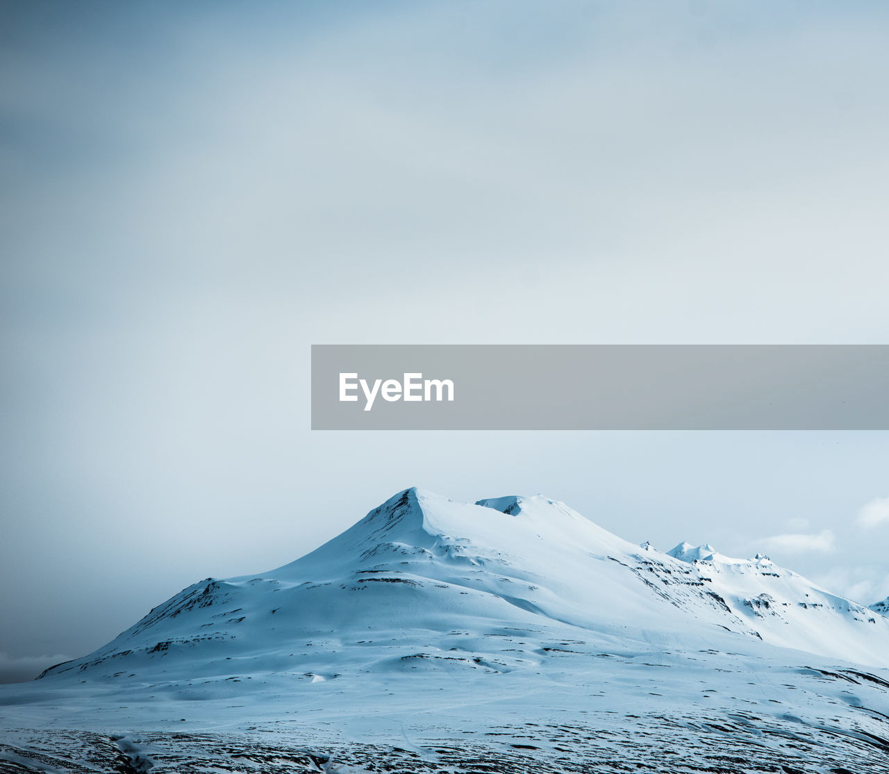 A snowy mountain peak with clouds behind it