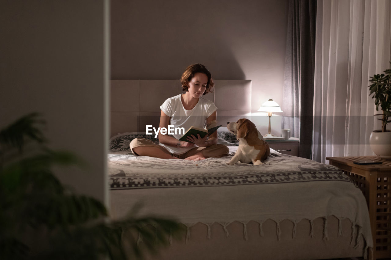 Woman reading book near dog in evening
