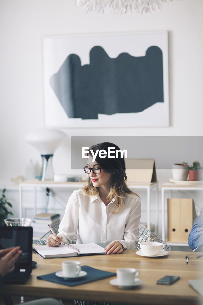 Smiling businesswoman writing while sitting at desk in office