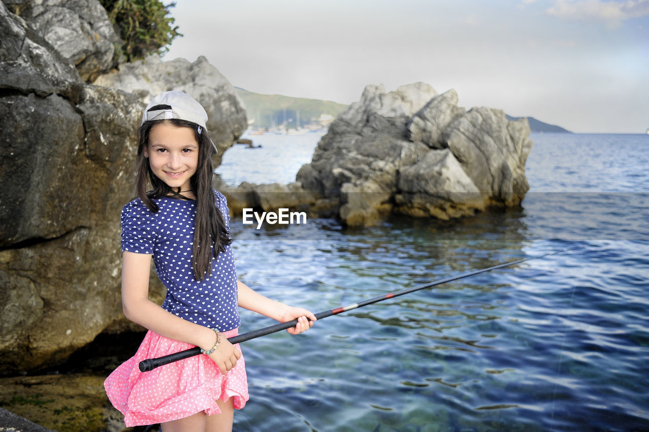 Portrait of happy girl fishing while standing at rocky beach