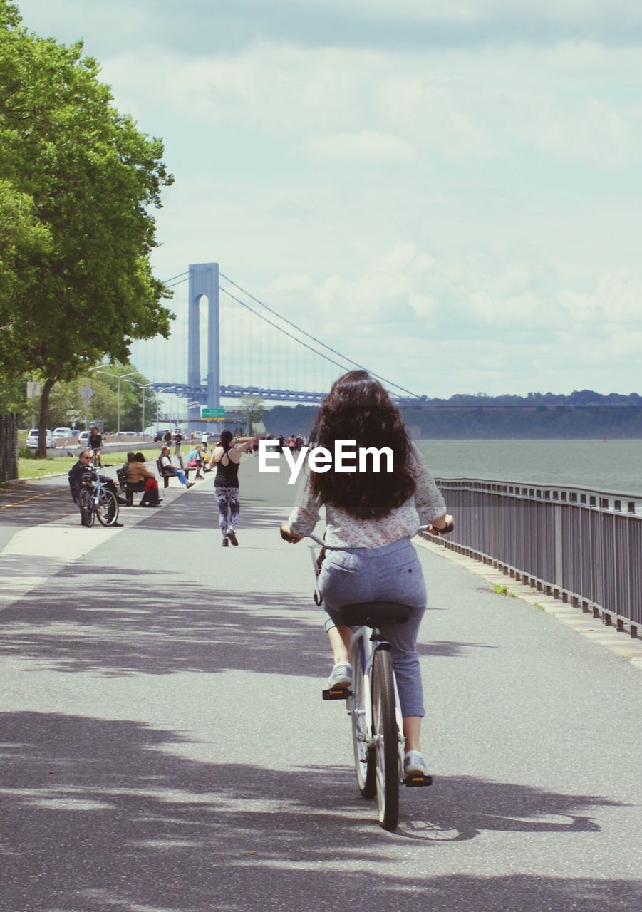 REAR VIEW OF WOMAN WITH BICYCLE AGAINST SKY IN CITY