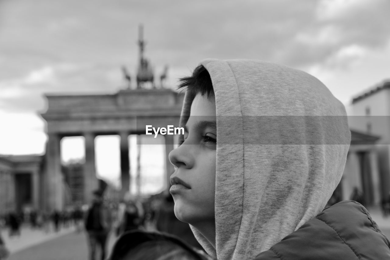 Close-up of thoughtful boy looking away against sky in city