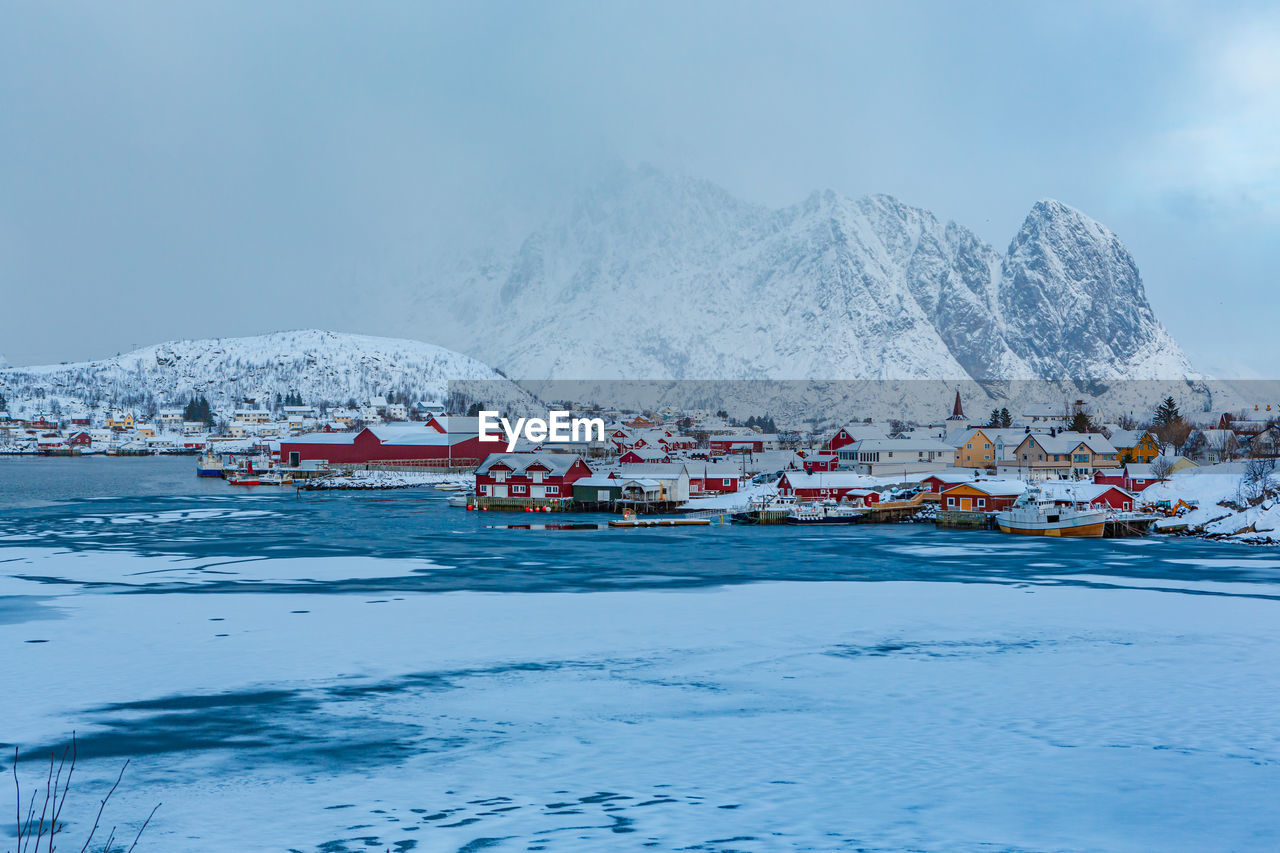 Scenic view of snowcapped mountains by town against sky during winter