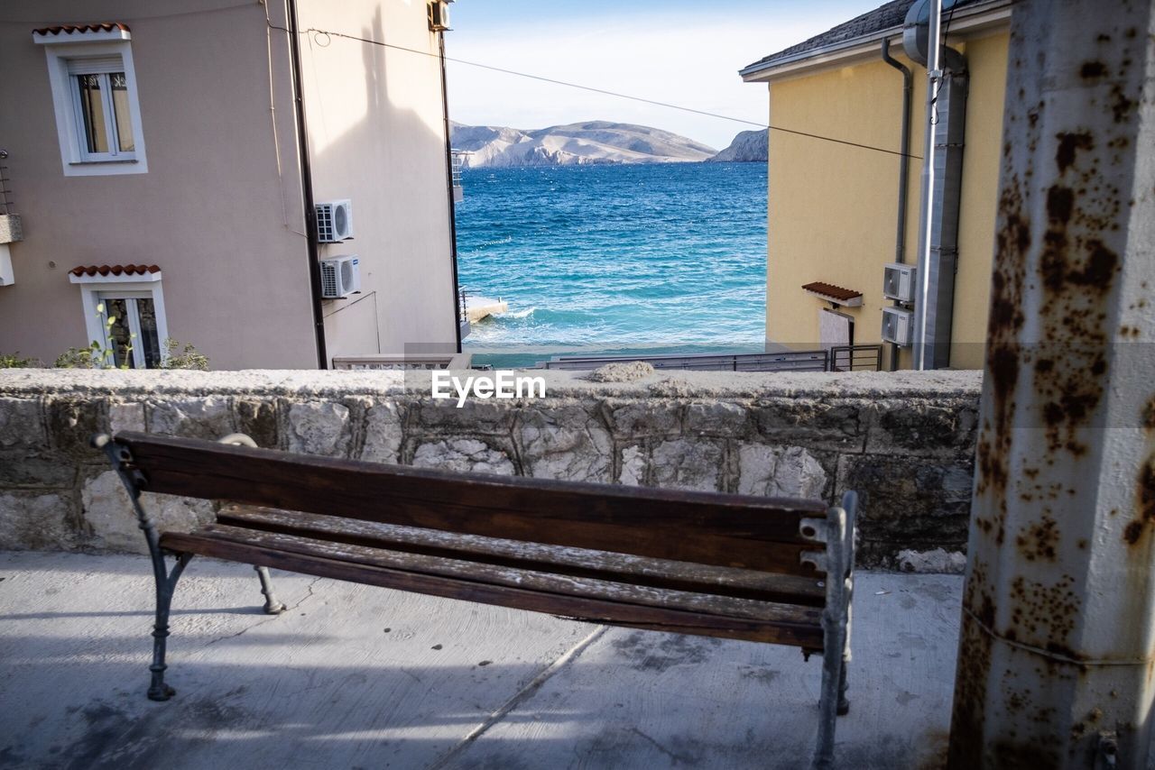 Empty bench on beach by sea against buildings