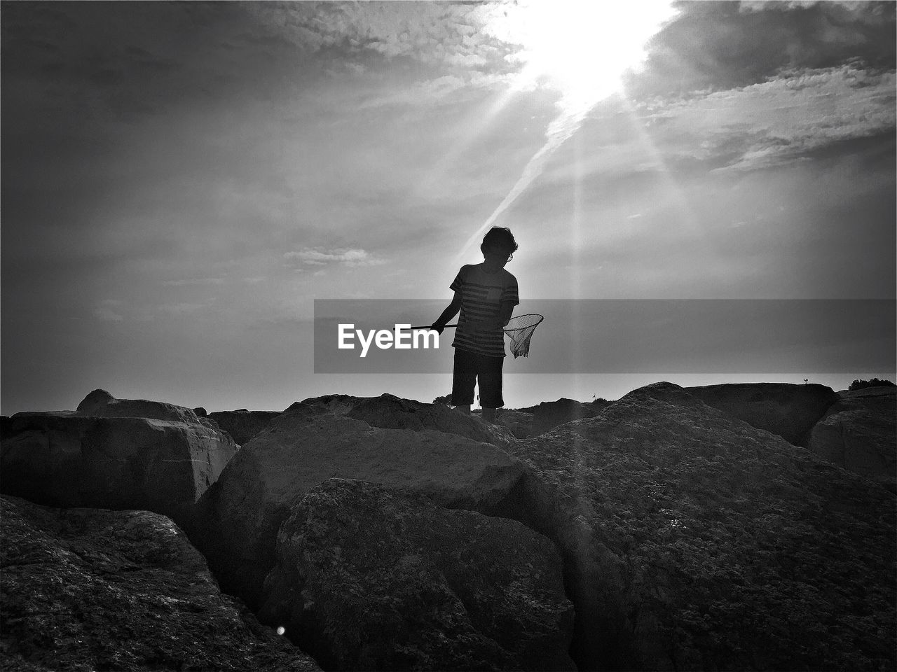 Boy standing on rock against sky