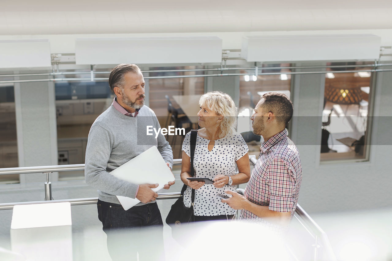 Businesspeople discussing by railing in modern office