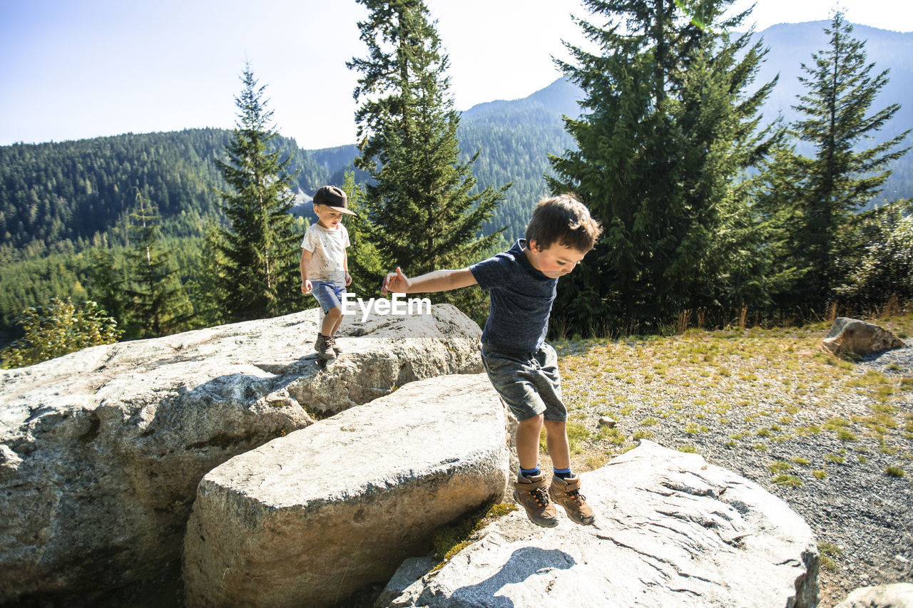 Young boys jumping, exploring on rocks in natural setting.