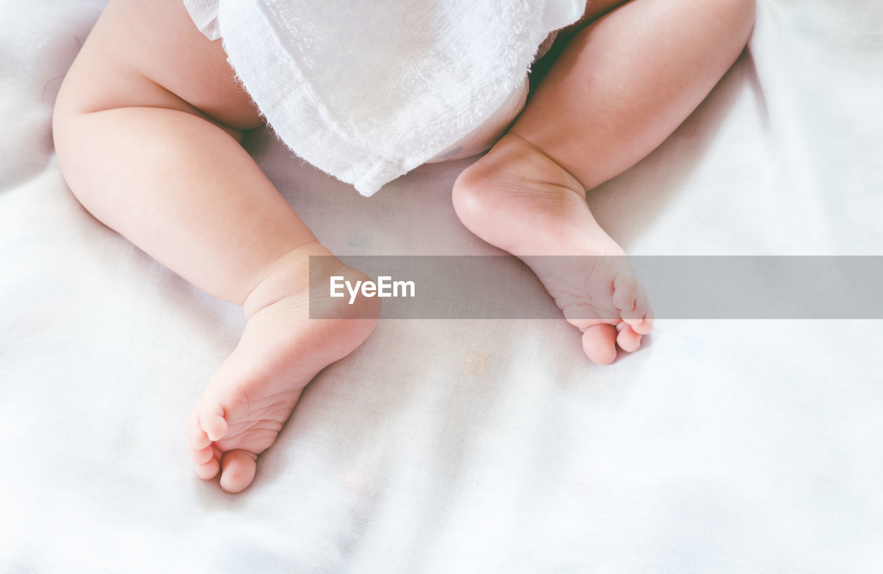 Low section of baby lying on bed