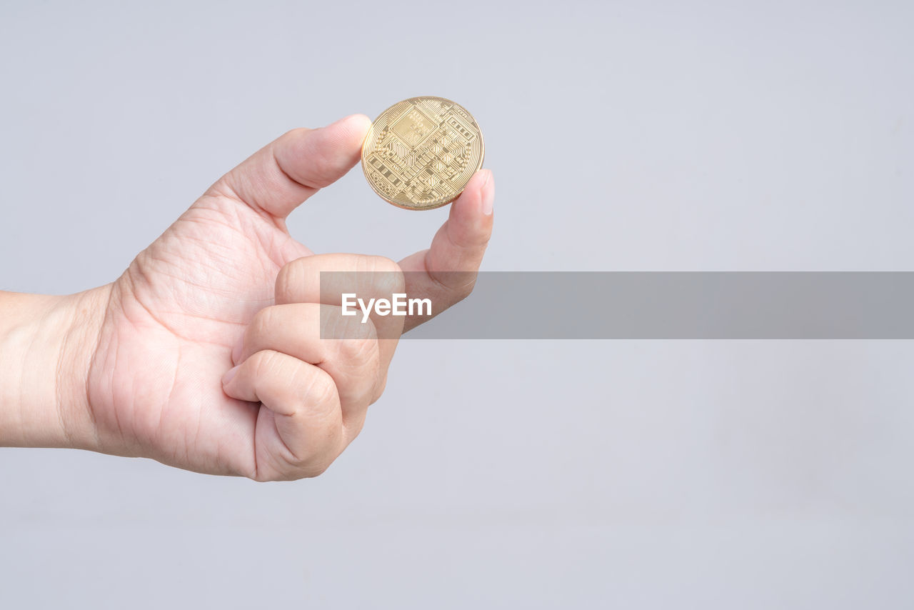 Cropped hand holding coin against gray background