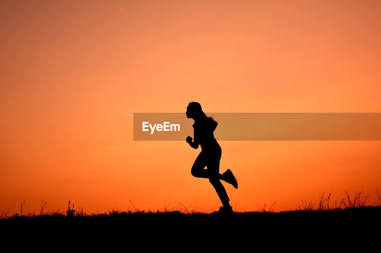 Silhouette of woman running on field at sunset