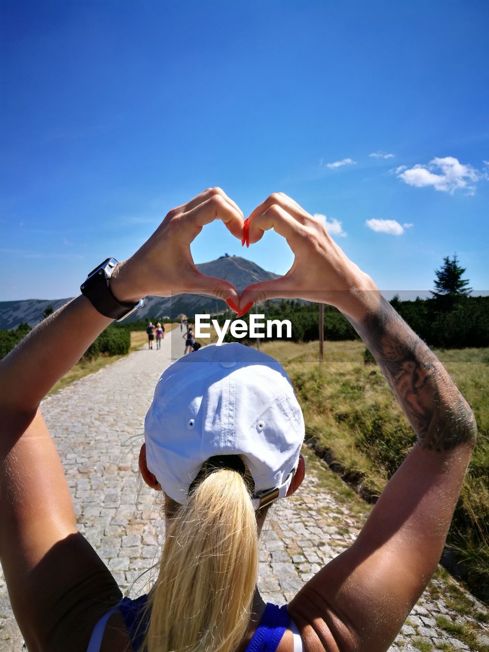 Rear view of woman making heart shape against sky