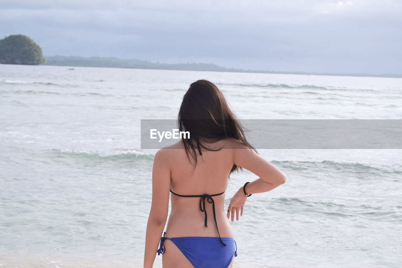 Rear view of woman in bikini standing at beach