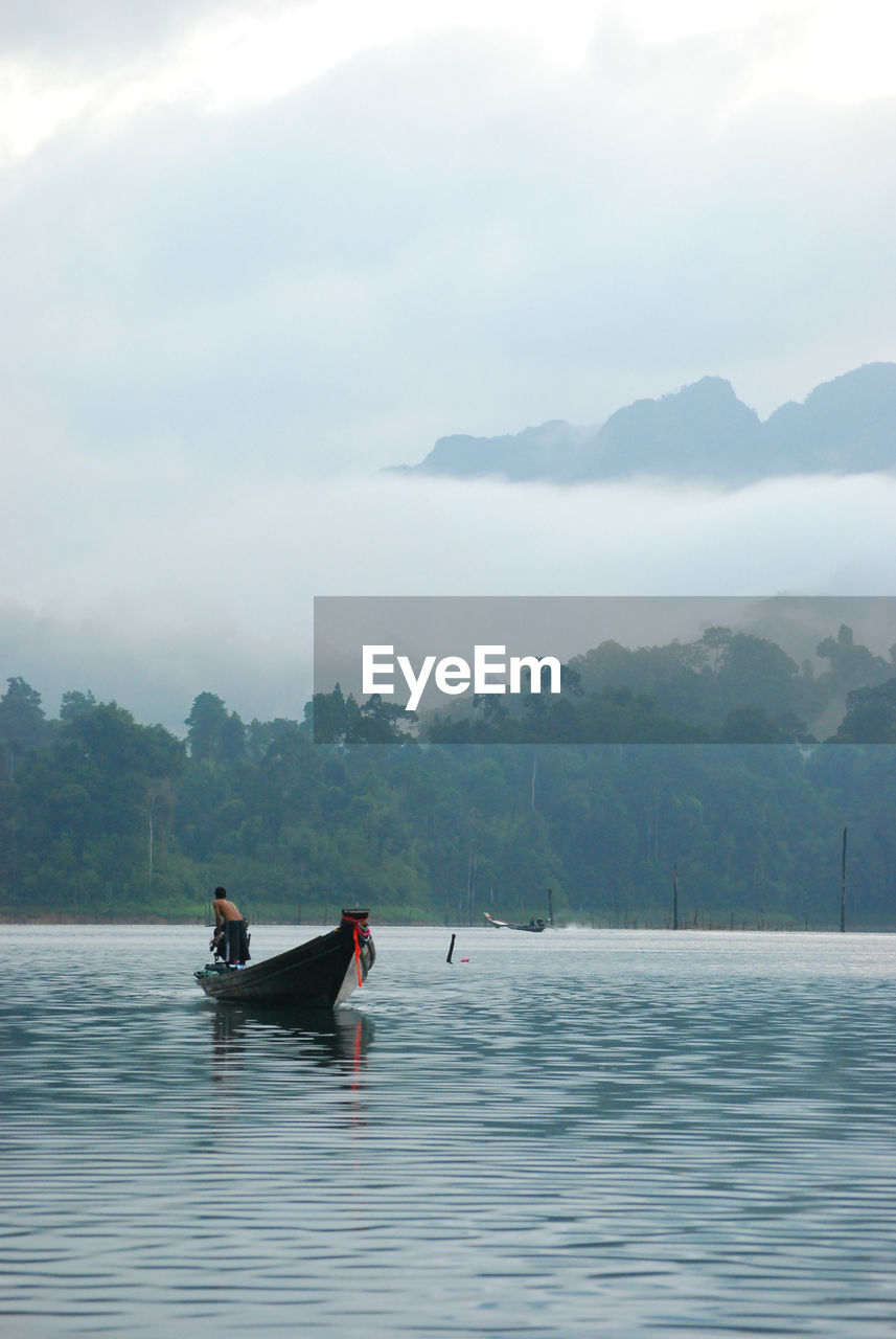 Man on longtail boat in lake against cloudy sky