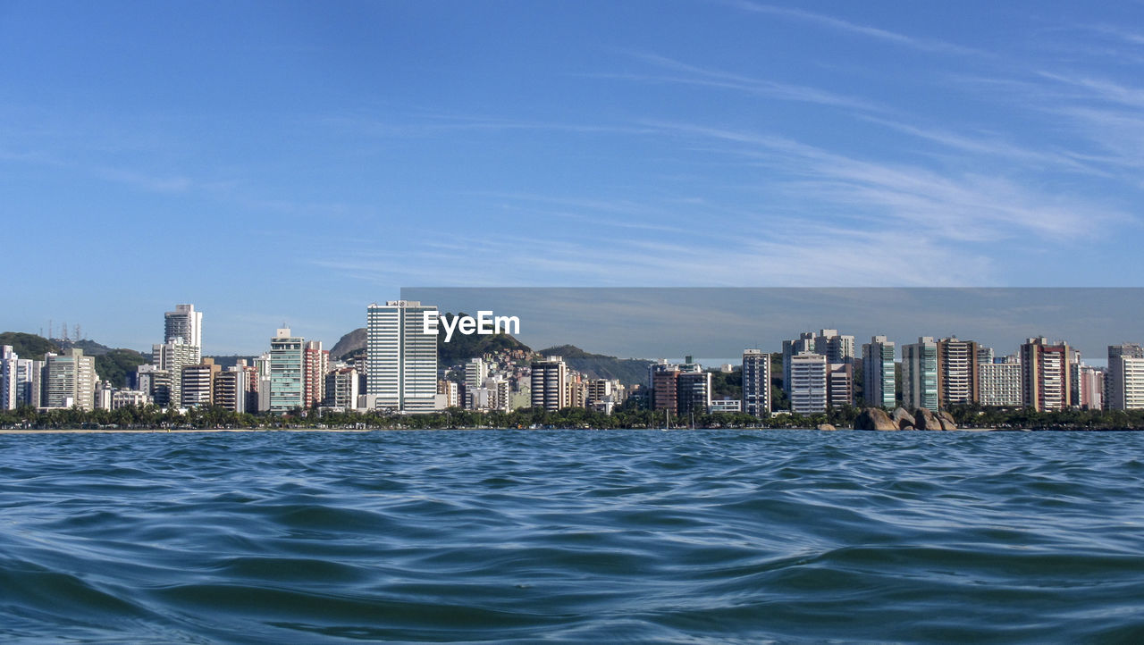 Sea by buildings in city against blue sky