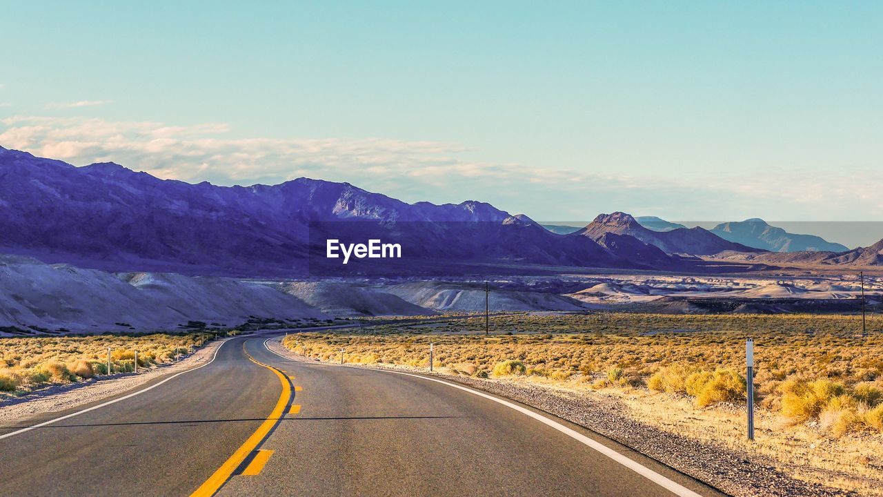 Empty road along landscape and mountains against sky