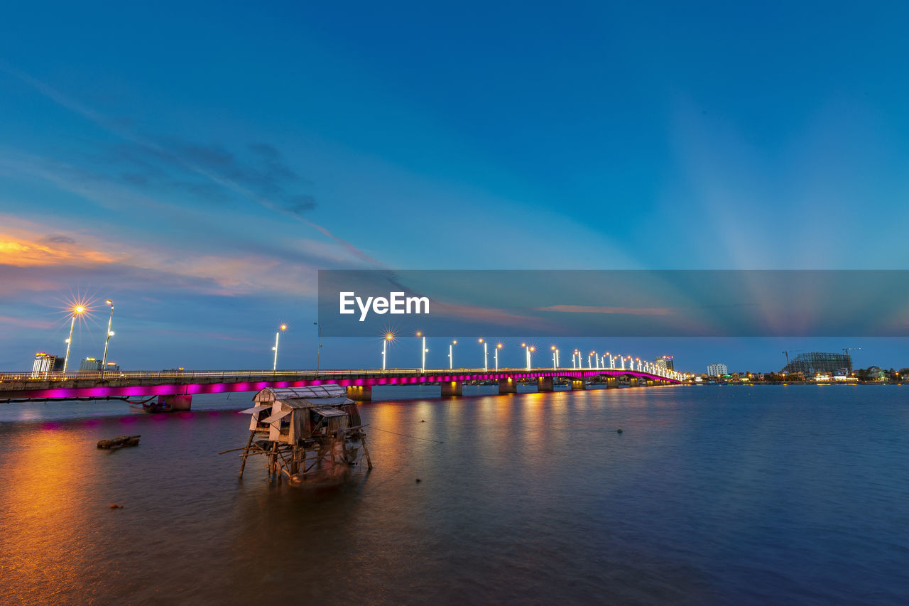 Illuminated city by sea against sky at night