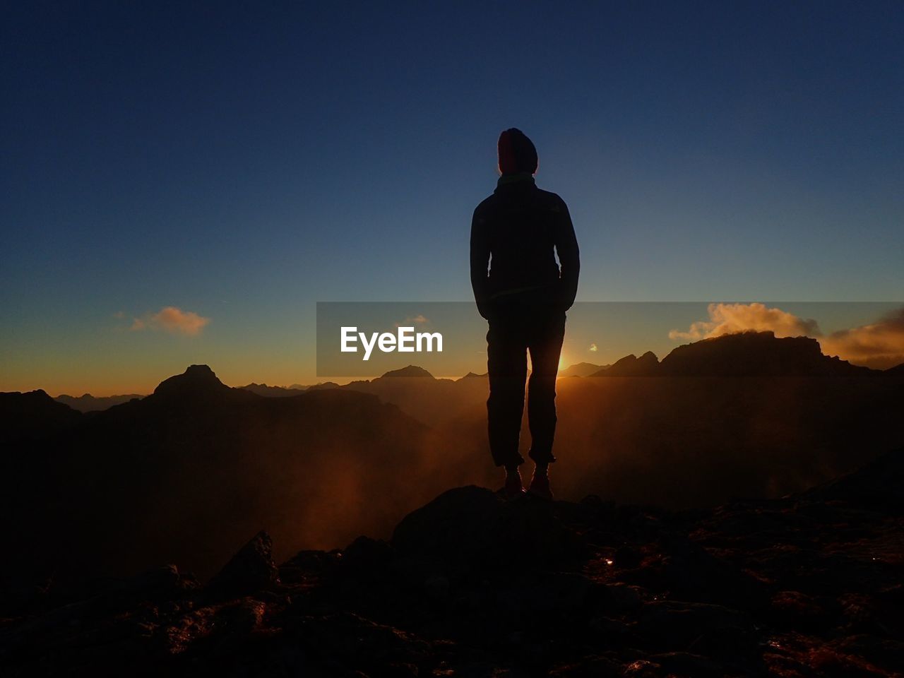 Rear view of silhouette man standing on mountain against sky