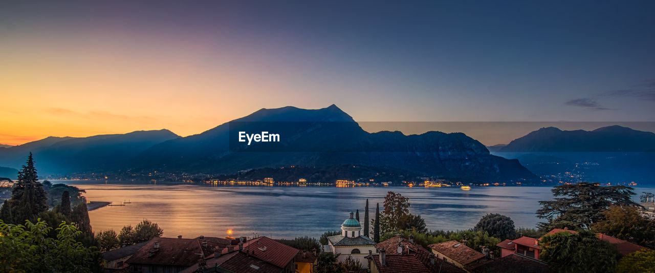 Scenic view of buildings by mountains against sky during sunset