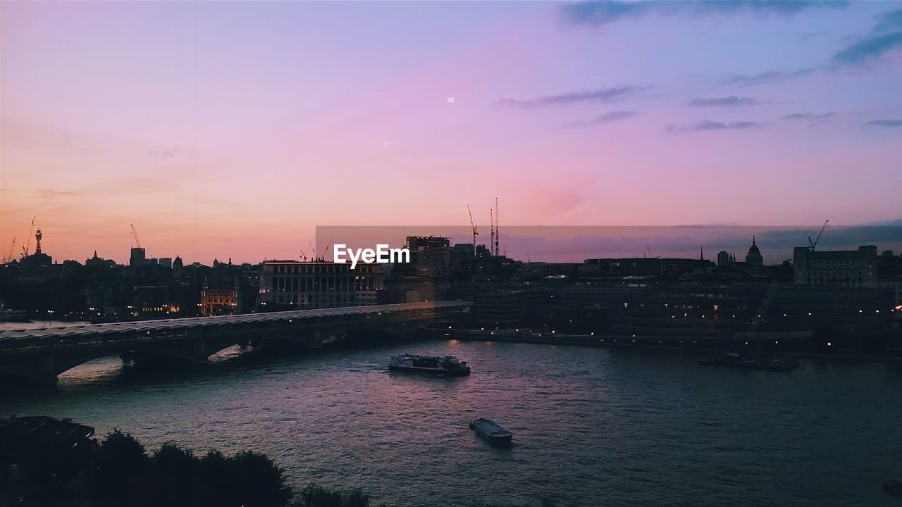 Bridge over thames river by city during sunset