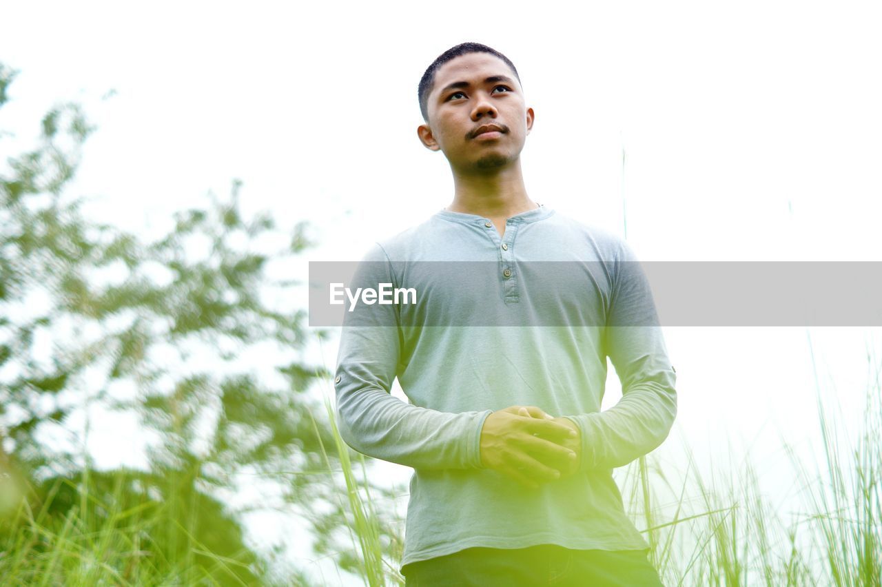 LOW ANGLE VIEW OF MAN LOOKING AWAY AGAINST PLANTS