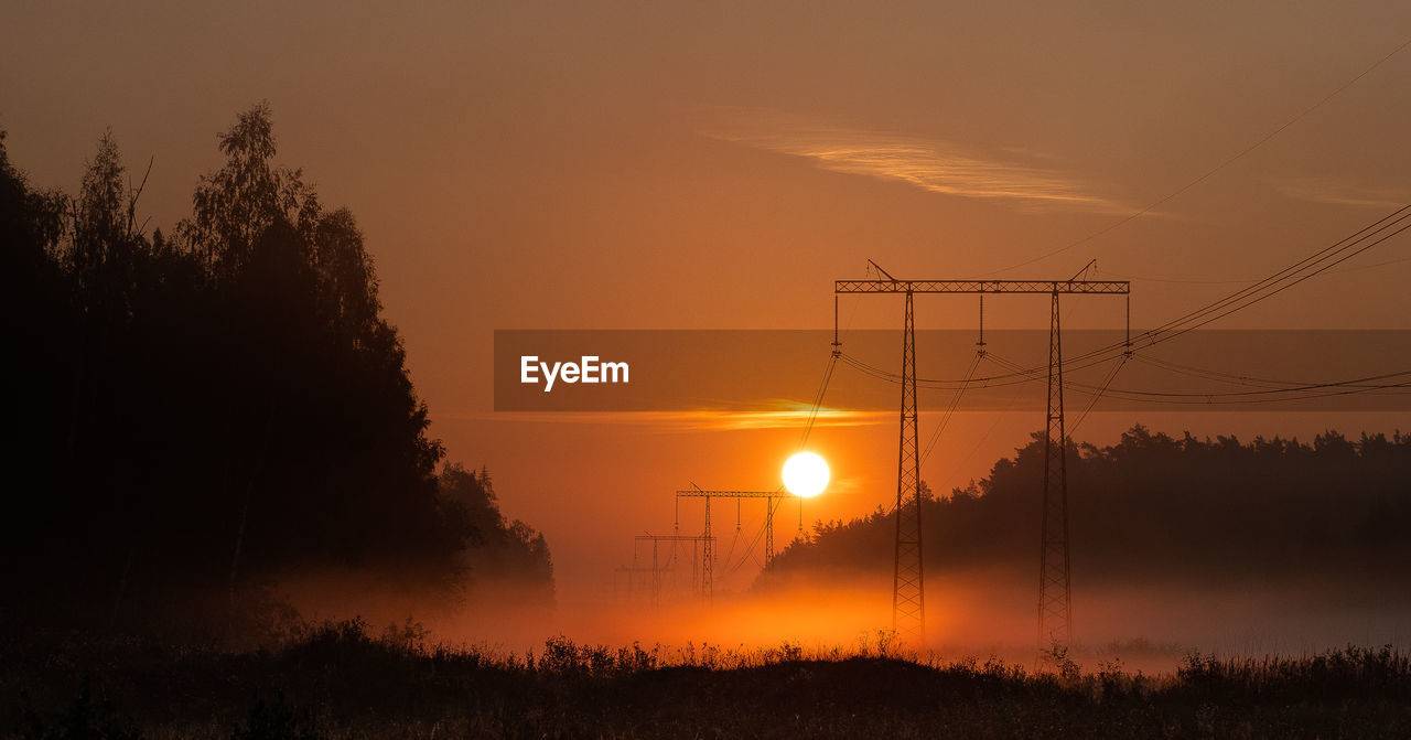 Silhouette trees and electricity pylon against sky during sunset