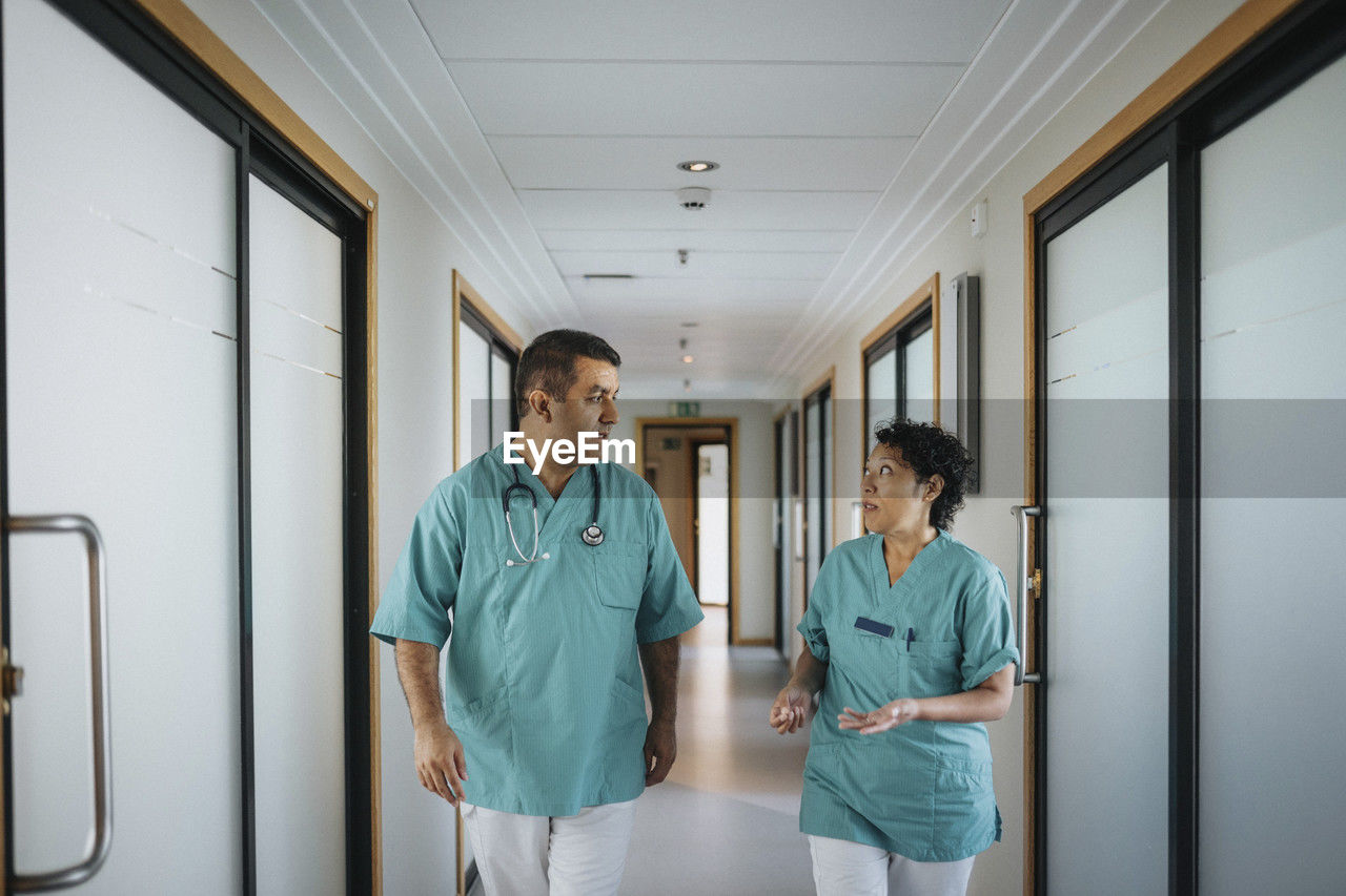 Multiracial male and female healthcare workers discussing while walking in corridor of hospital