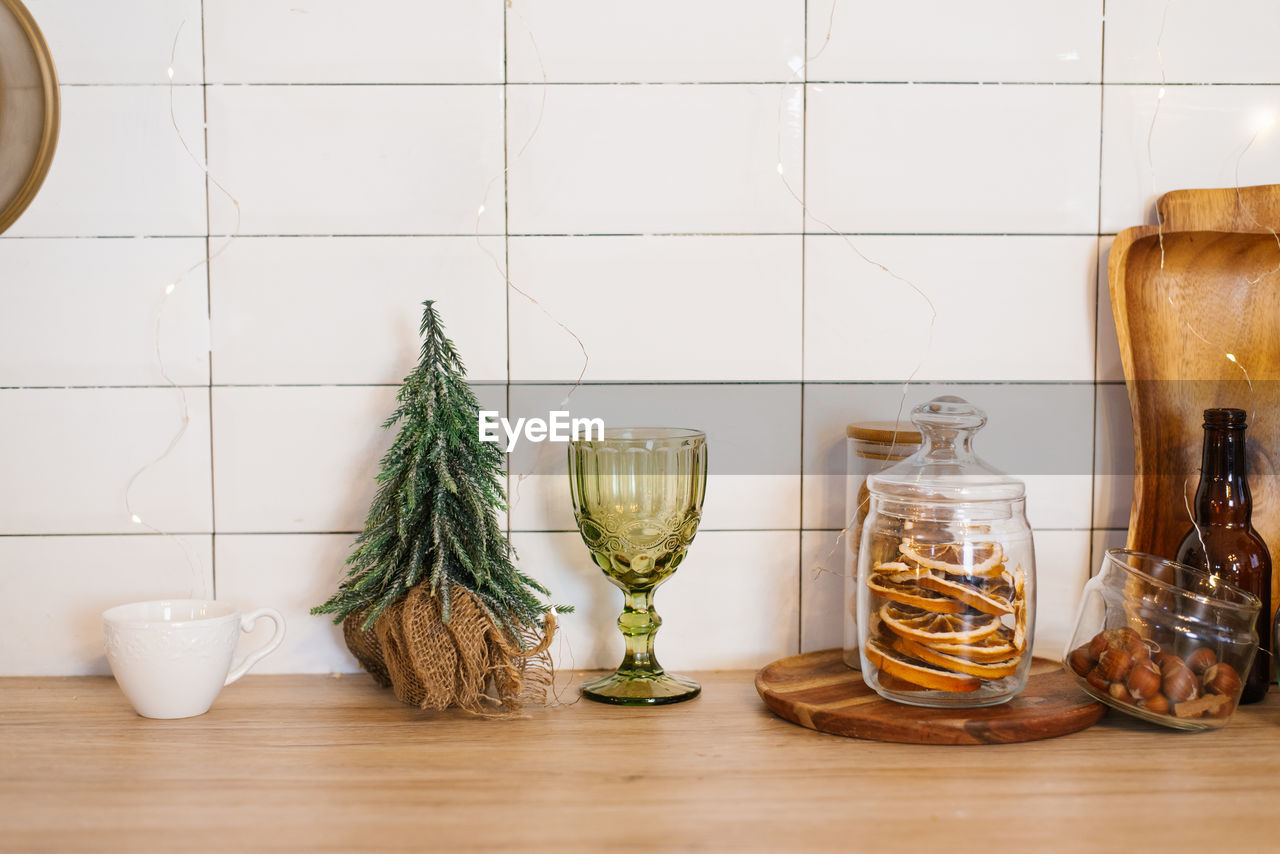 Christmas tree is on a counter next to a wine glass and a jar of nuts. cozy and festive