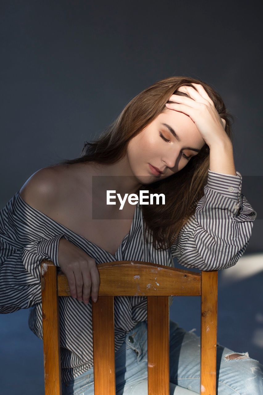 Thoughtful young woman with eyes closed sitting on chair