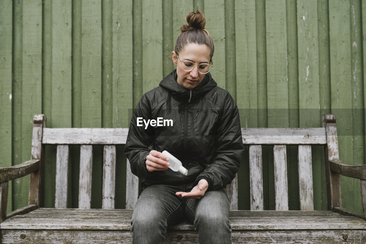 Woman on bench applying antibacterial gel on her hands