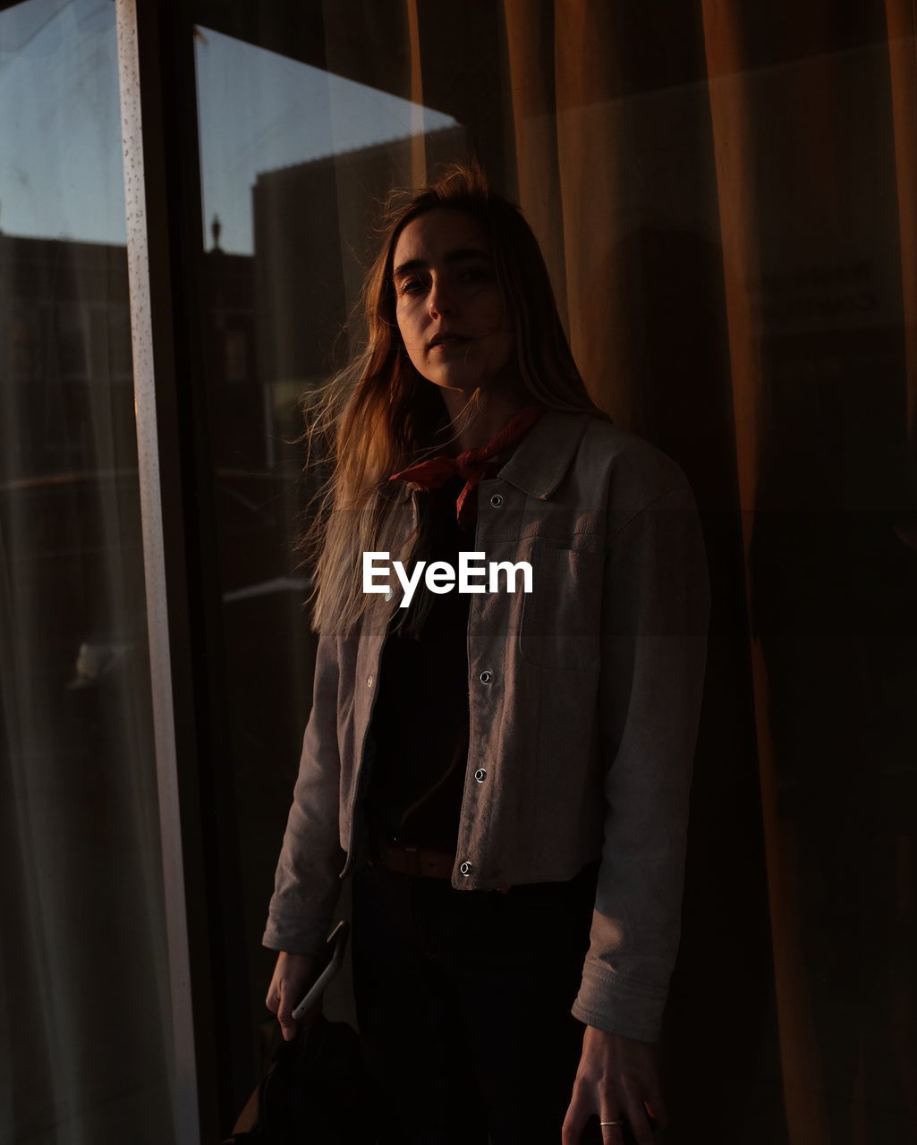 Portrait of young woman standing by window at home