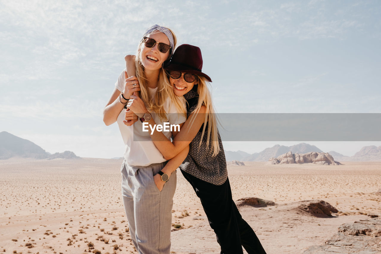 Happy friends wearing sunglasses standing on desert against sky