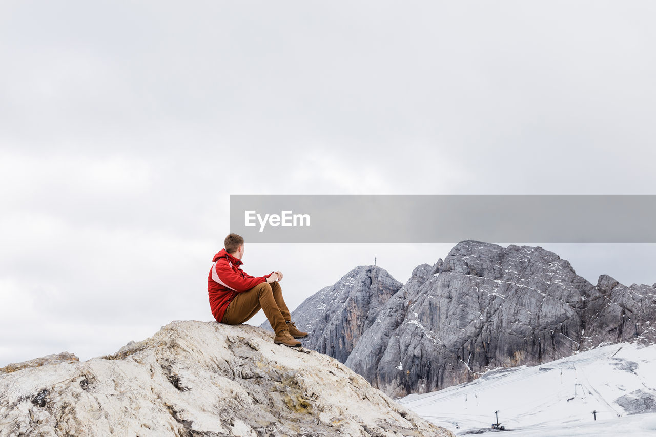 Young millennial man enjoys the views of the alps standing on glacier