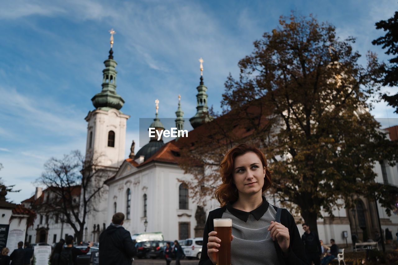 Woman holding beer against building in city