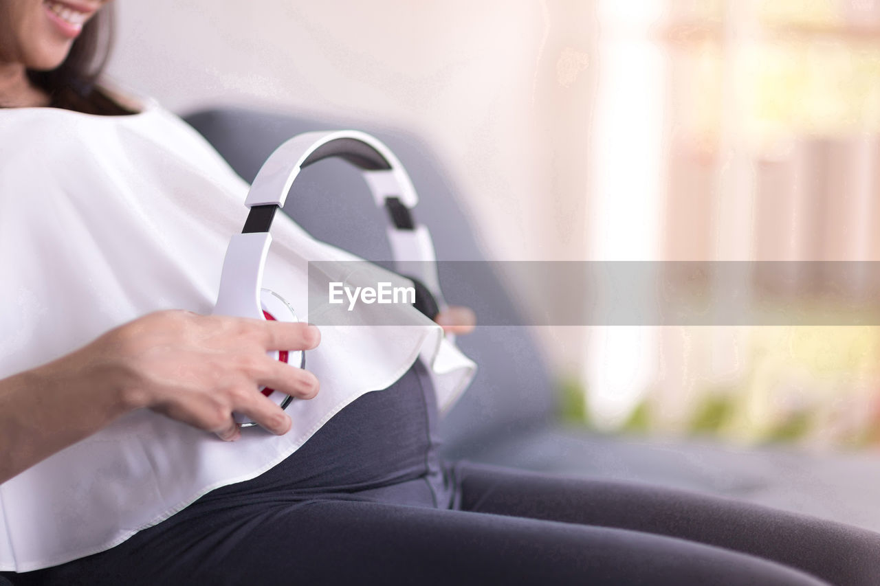 MIDSECTION OF WOMAN USING SMART PHONE WHILE SITTING ON MOBILE