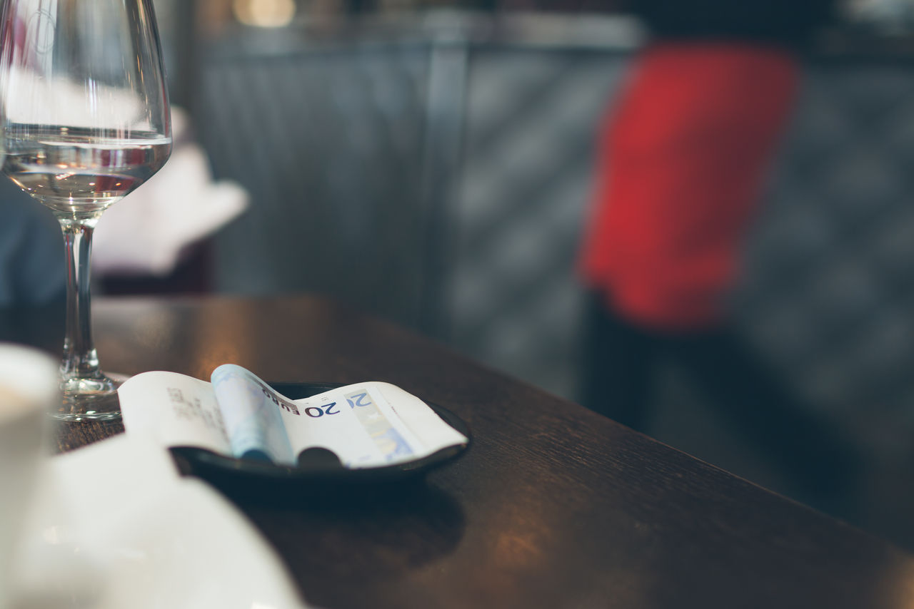 Close-up of glass and receipt on table with midsection of person in background at restaurant