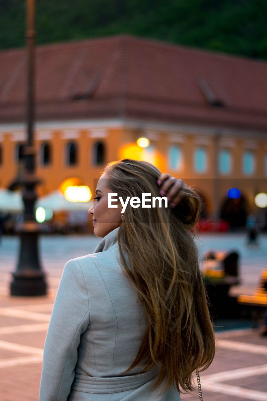 Young woman with long hair standing on walkway in city at dusk