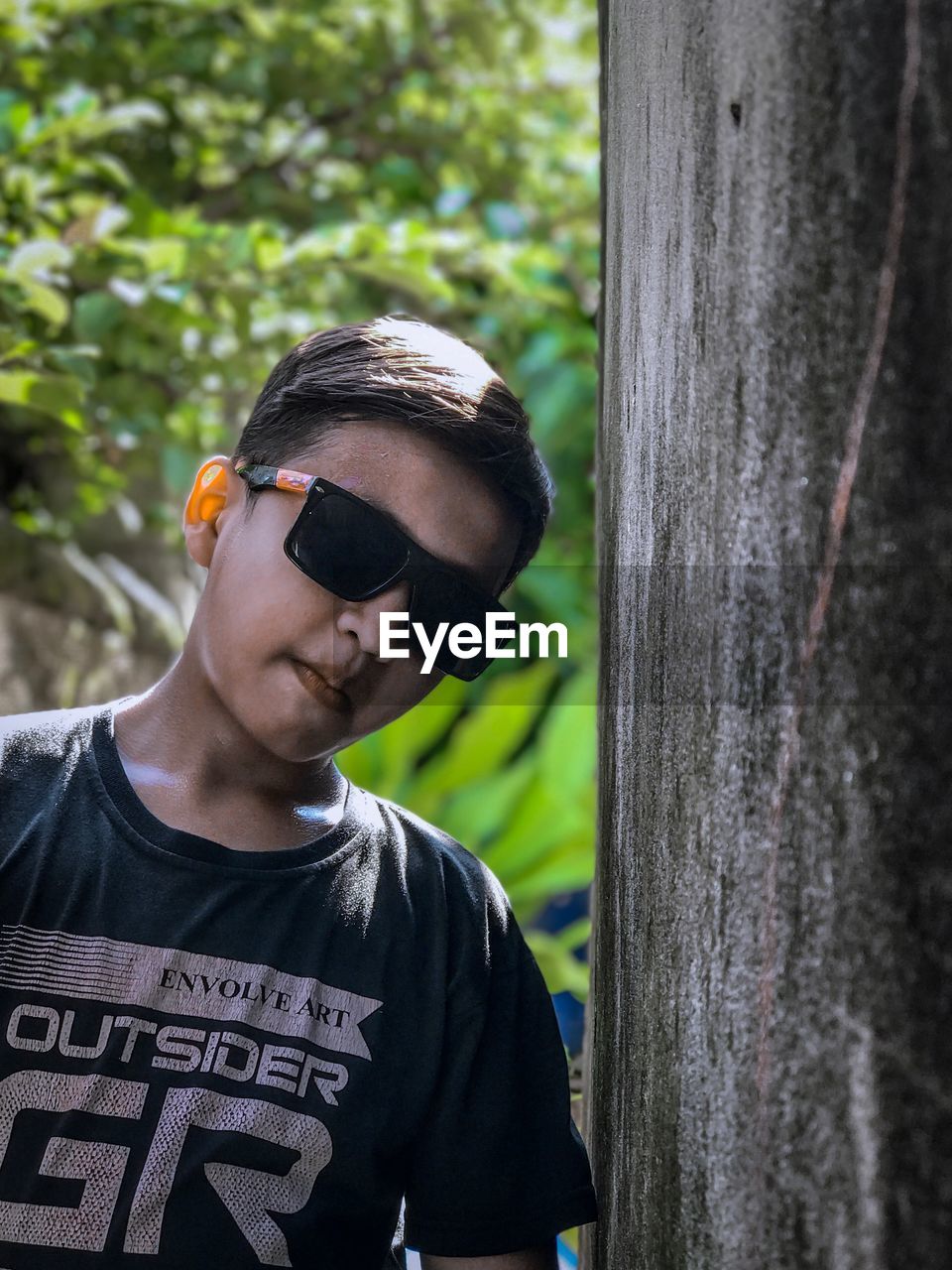 Portrait of boy wearing sunglasses standing by tree trunk