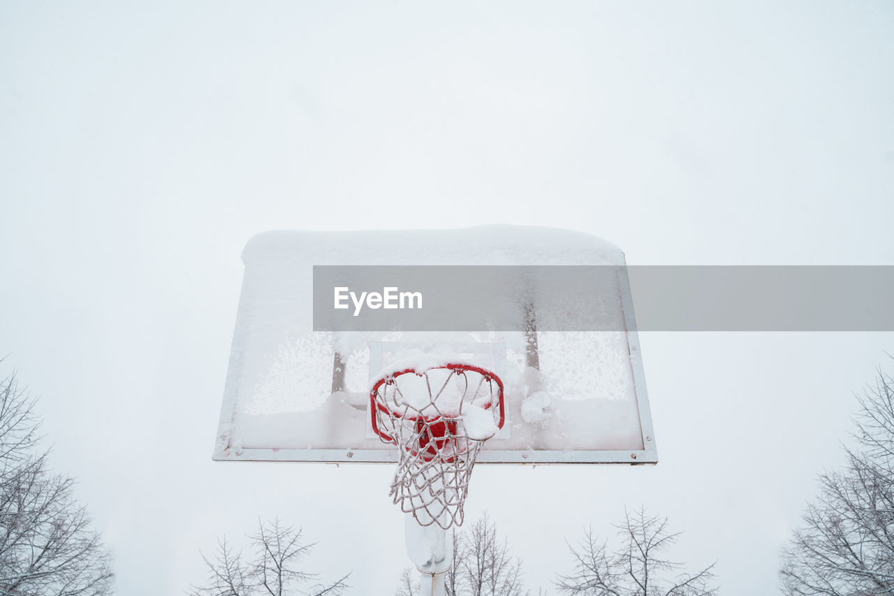 LOW ANGLE VIEW OF BASKETBALL HOOP AGAINST TREES DURING WINTER
