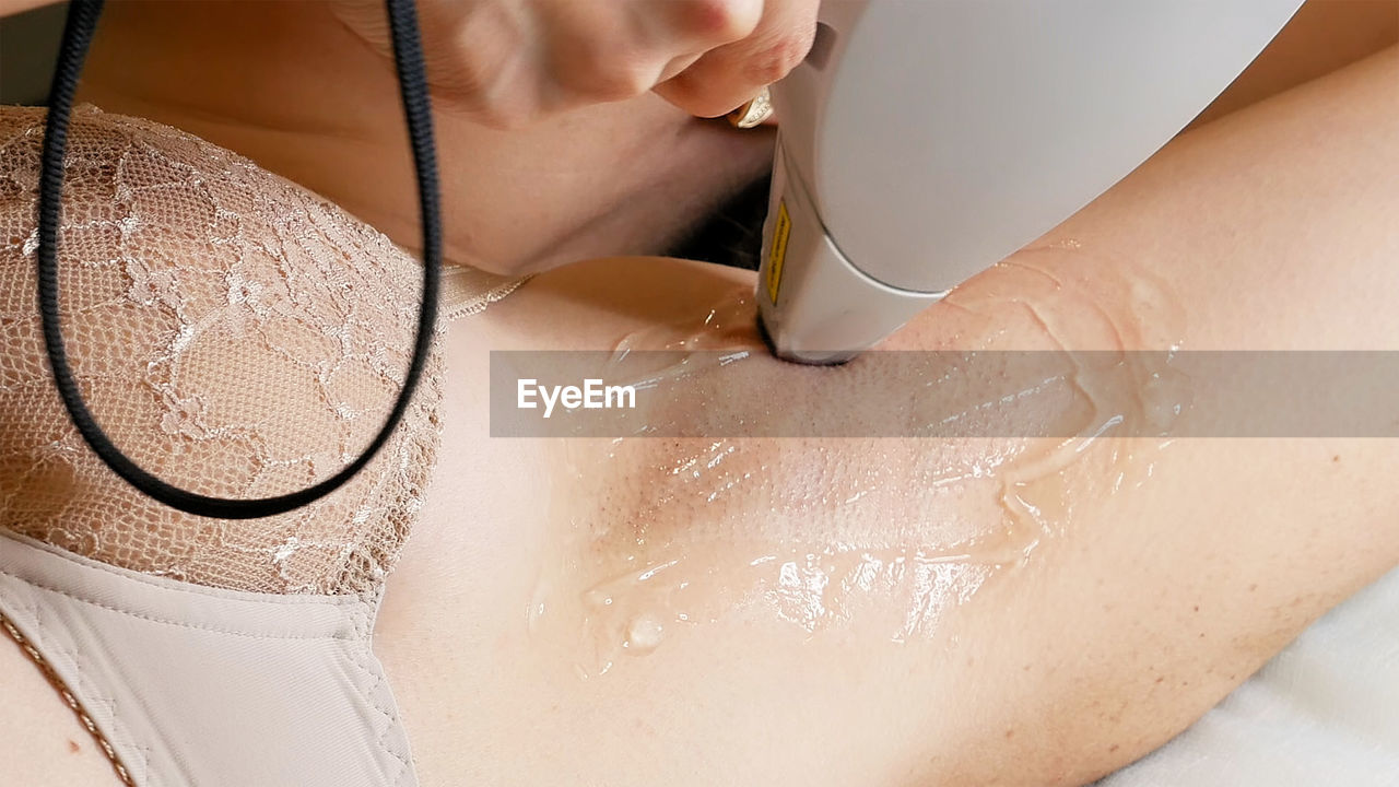 Cropped hand of woman applying gel on female customer armpit in spa